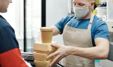 Man Wearing a Face Mask Putting Food on a Thermal Bag